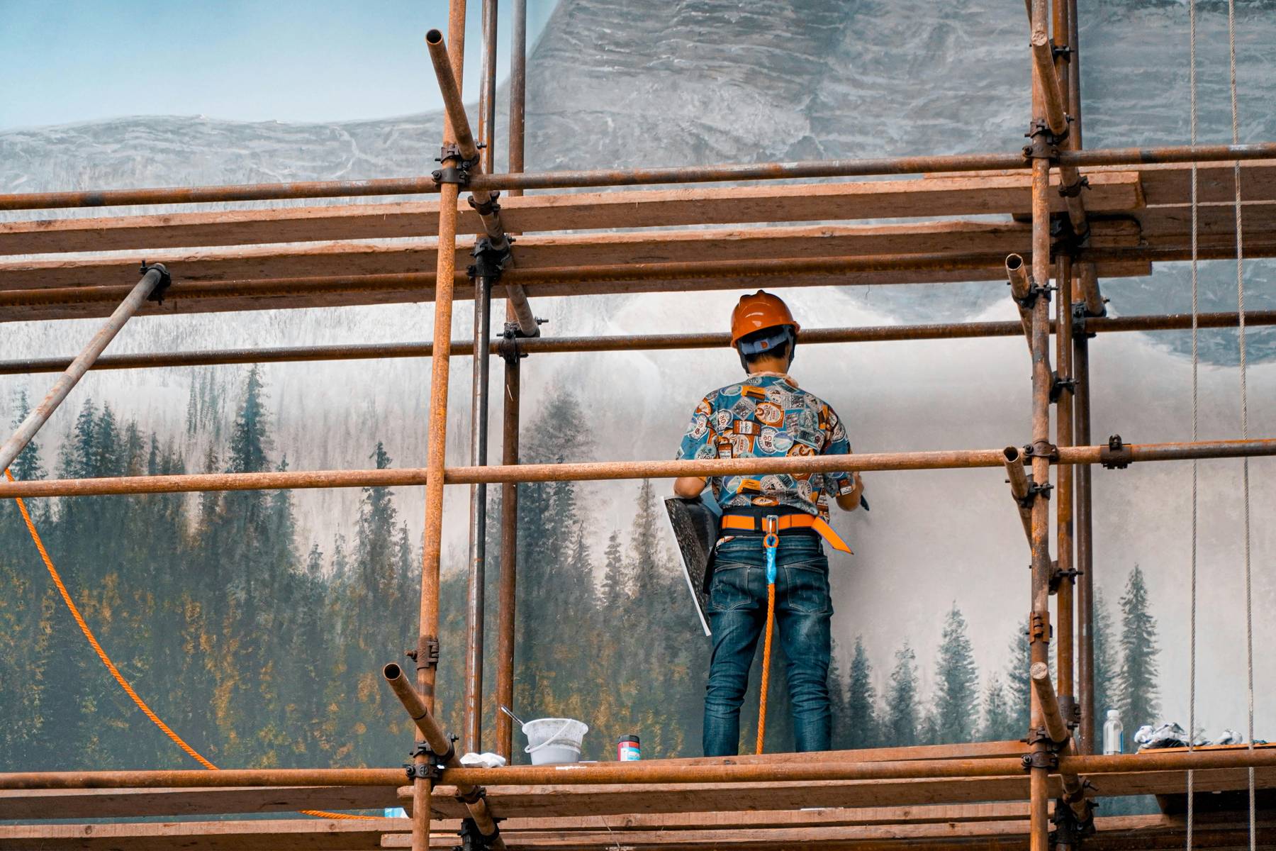 a worker on scaffolding, secured by a safety harness and wearing a hard hat